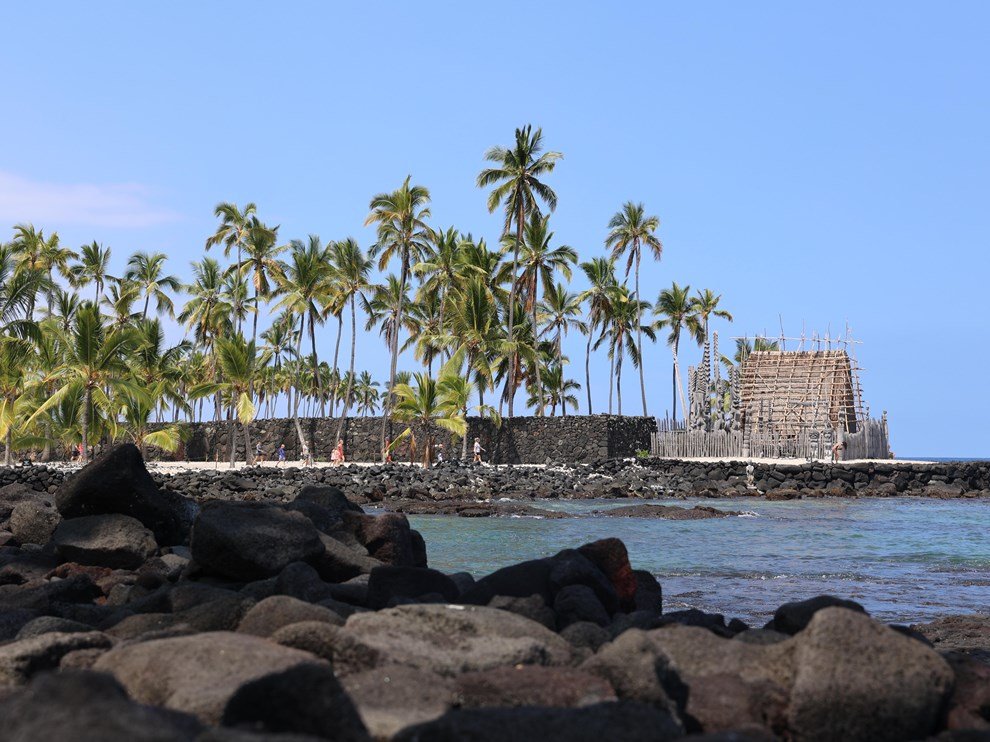 Sacred temple and coconut trees next to the ocean as viewed from a rocky wall across the bay.